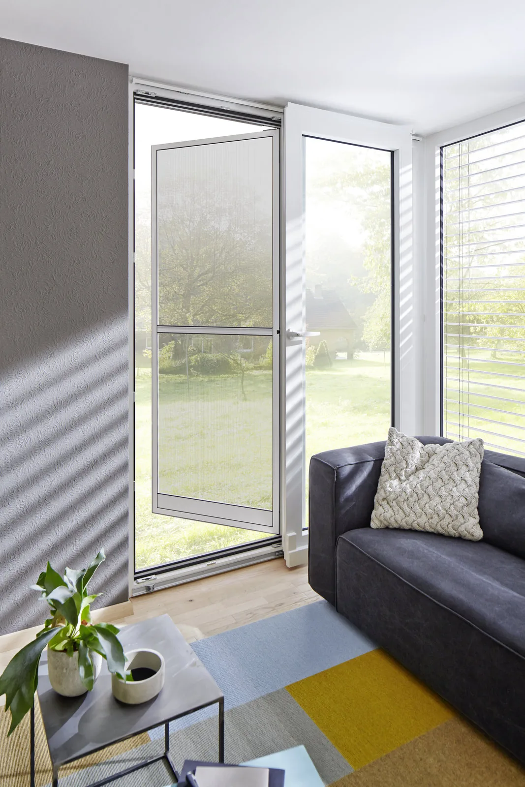 Weiße Kunststoff-Balkontür im Wohnzimmer mit Blick in den Garten
